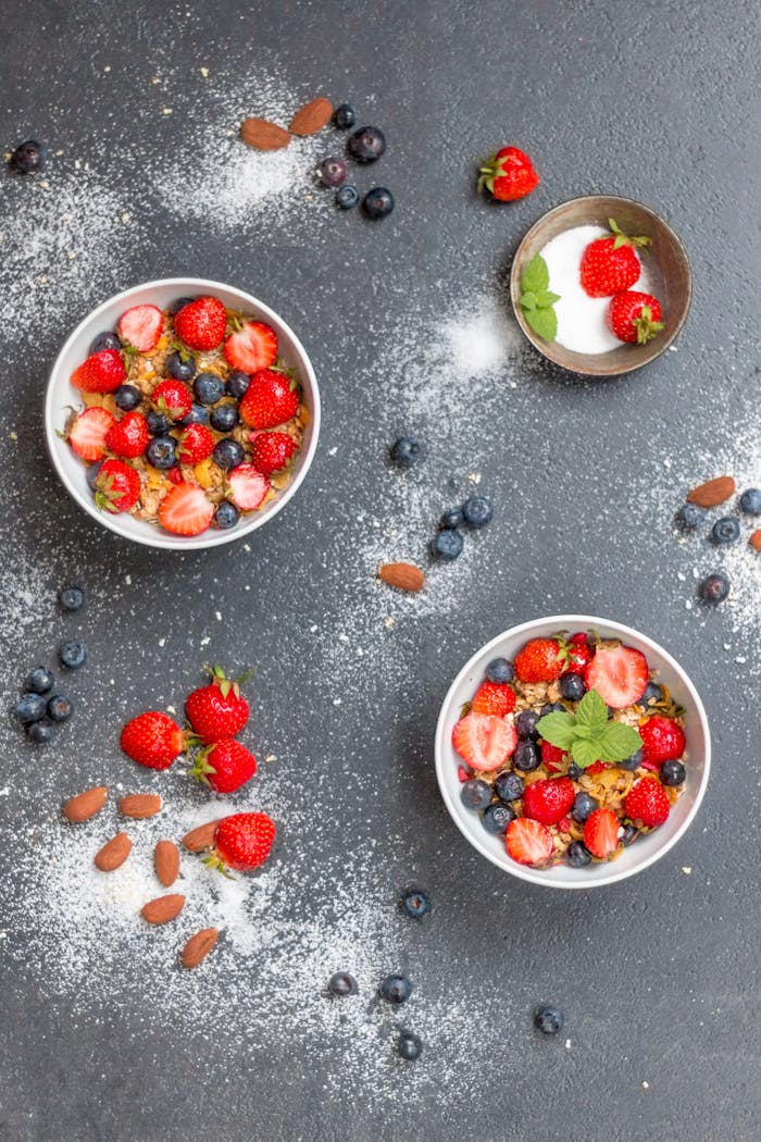 Top view of bowls filled with cereal, strawberries, and blueberries, perfect for a healthy breakfast.
